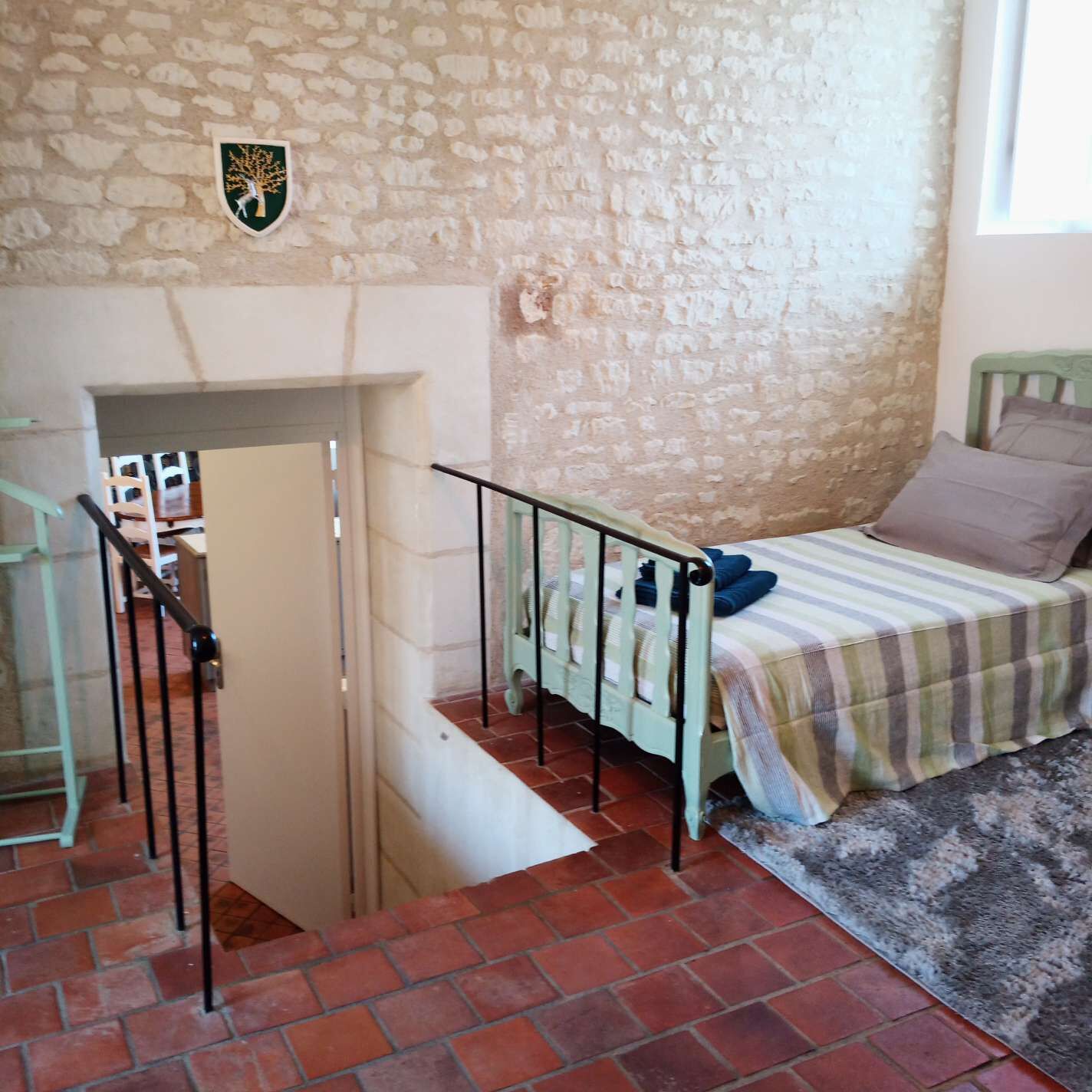 Un dormitorio con pared de piedra, una cama con manta a rayas y una barandilla de metal.