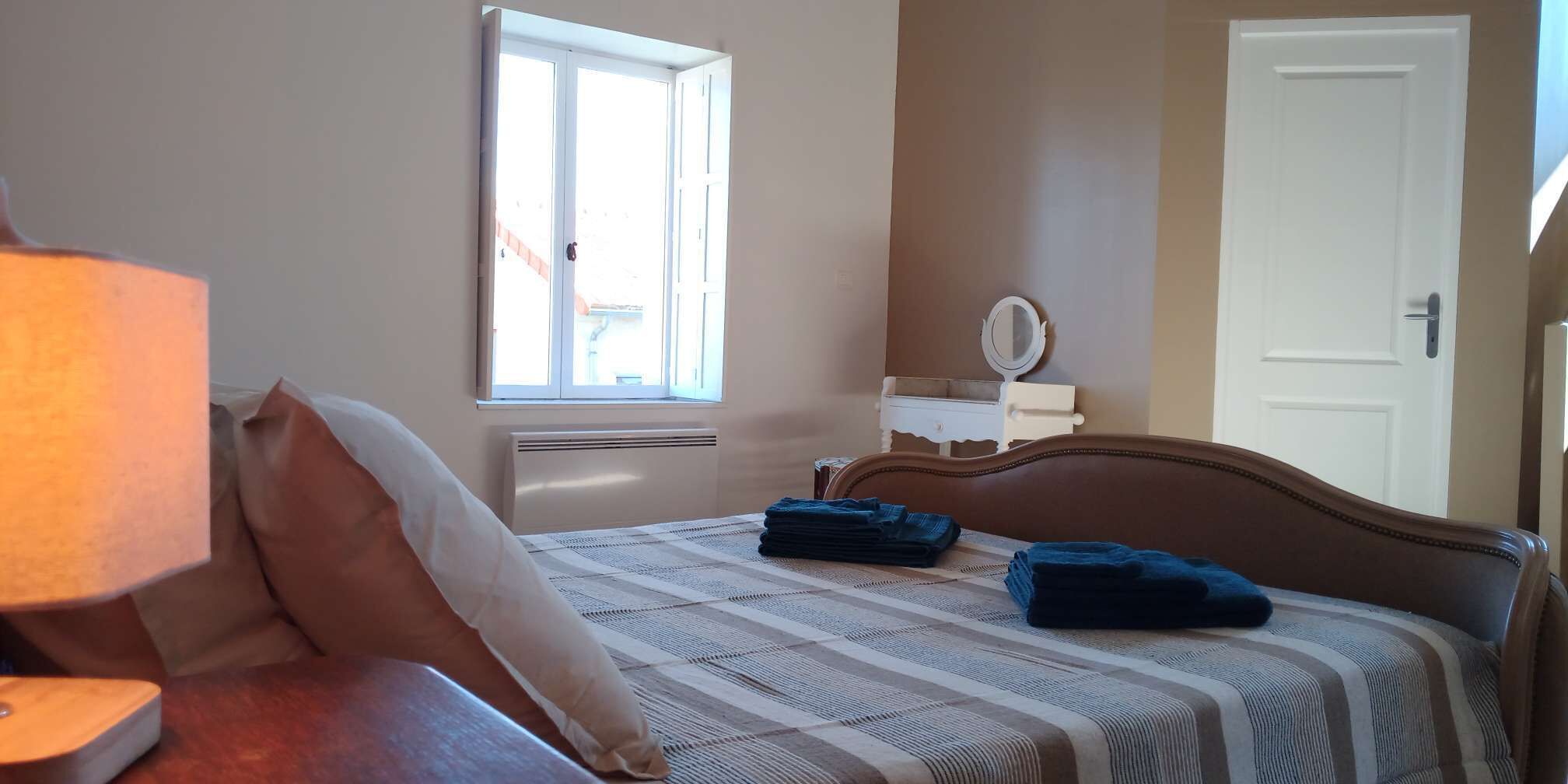 Une chambre à coucher avec un lit, une table de chevet avec une lampe, une fenêtre, un miroir et une porte.