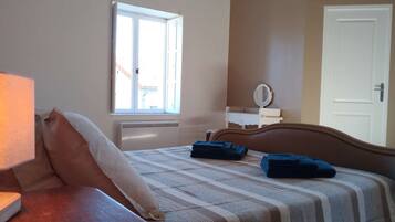 Une chambre à coucher avec un lit, une table de chevet avec une lampe, une fenêtre, un miroir et une porte.
