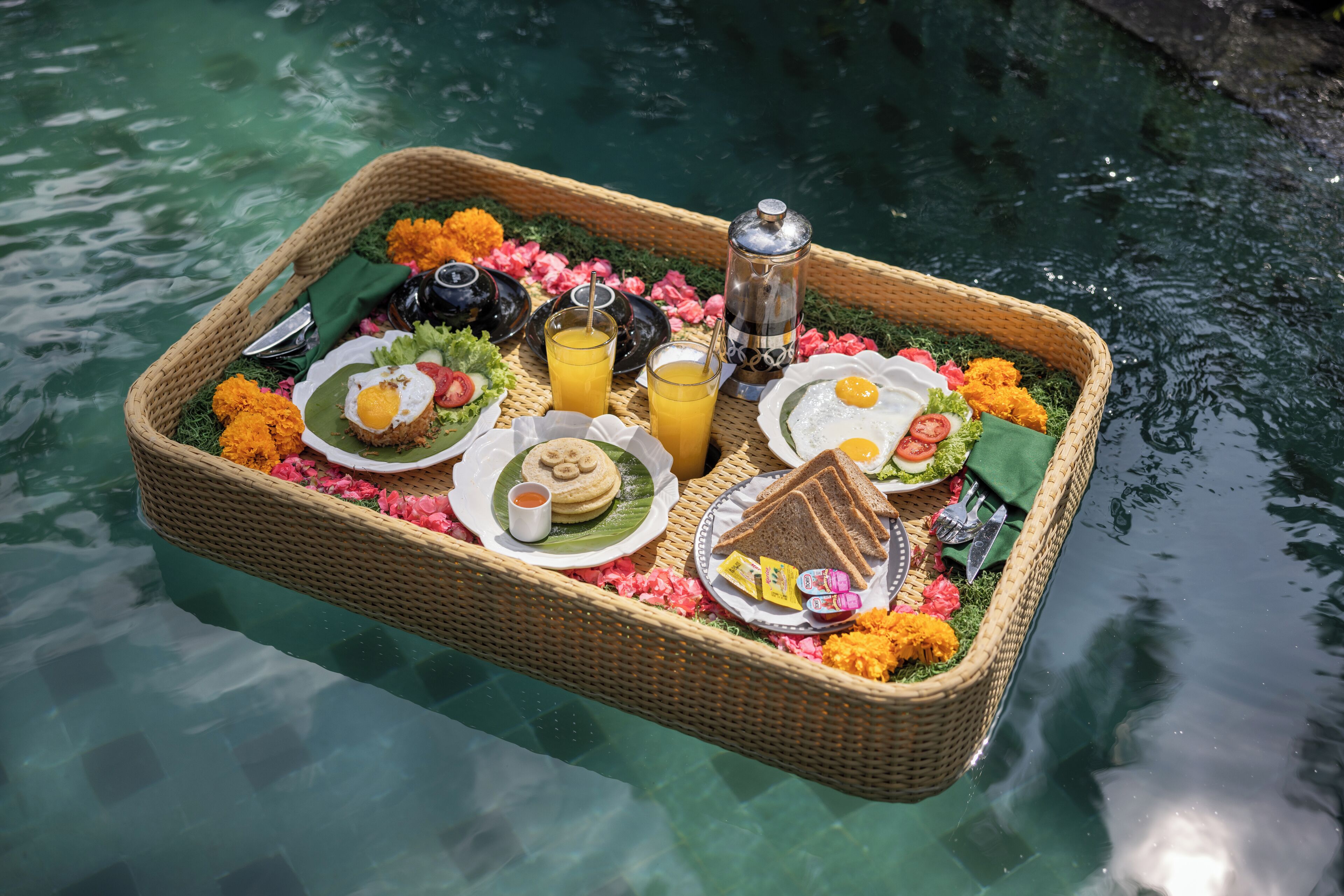 A floating dining setup with a wicker tray containing food and drinks, surrounded by water.