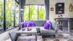 Un salon moderne avec un canapé gris, des coussins violets, une table basse et une bibliothèque noire.