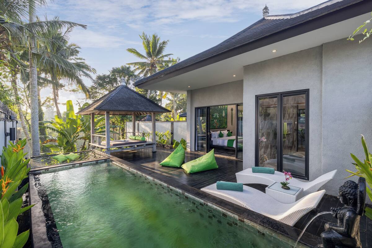 A modern house with a swimming pool, green cushions, and a statue.