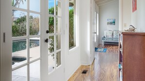 A hallway with a wooden floor, a white door, and a view of a pool and greenery outside. - Pool, Foosball, Pool Table, Basketball Family Friendly, blocks from the beach! (San Diego)