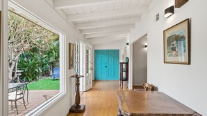 A hallway with a wooden floor, a dining table, chairs, and a bright blue door at the end. - Pool, Foosball, Pool Table, Basketball Family Friendly, blocks from the beach! (San Diego)
