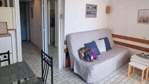 A compact room with a bed, a small table, and a chair. There is a doorway leading to a bathroom.