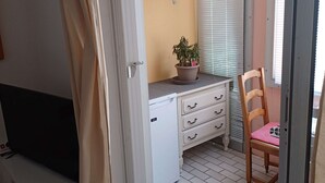 A room with a white desk, a chair, a potted plant, and a window with blinds.