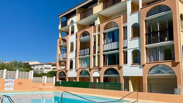 A multi-story hotel with balconies, a swimming pool, and a clear blue sky.