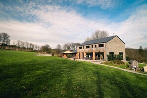 Une grande maison moderne à deux étages, avec une façade en pierre et une vaste véranda à l’avant.