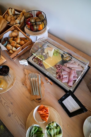 Noutopöytä, jossa on tarjolla monenlaista ruokaa, kuten leipää, hedelmiä, juustoja ja lihatuotteita.