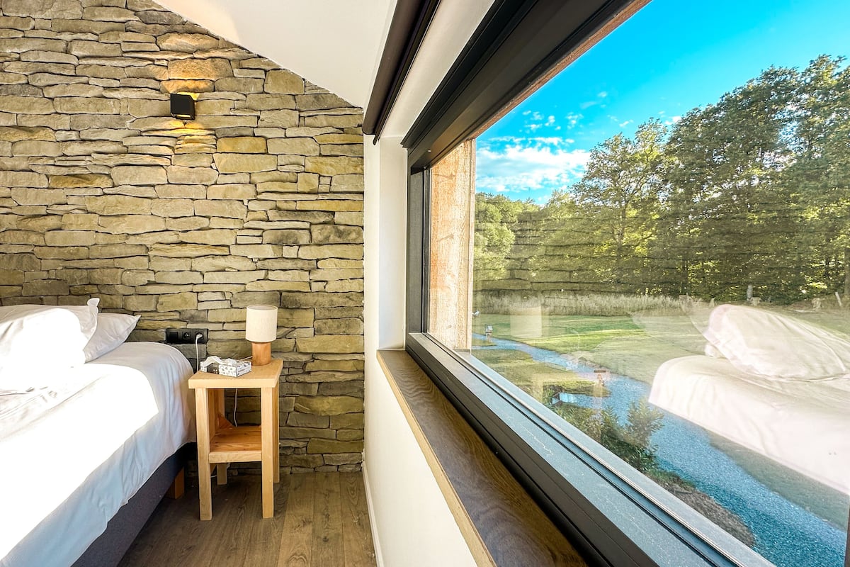 Une chambre avec des murs en pierre, une table de chevet en bois, deux lits et une fenêtre donnant sur un jardin.