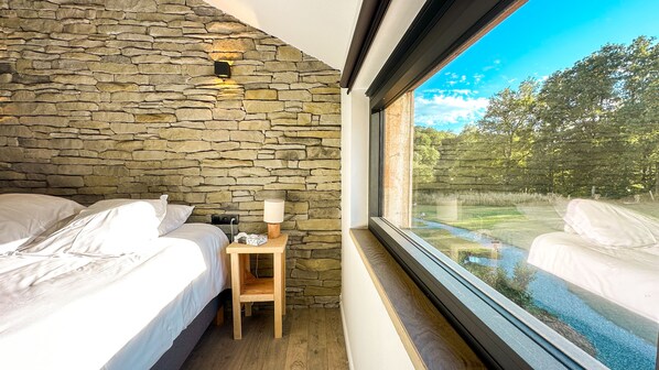 Une chambre avec des murs en pierre, une table de chevet en bois, deux lits et une fenêtre donnant sur un jardin.
