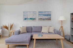 Una sala de estar moderna con un sofá seccional gris, una mesa de centro de madera y dos cuadros enmarcados con barcos en la pared.
