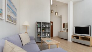 Una sala de estar moderna con un sofá, una mesa de centro, un televisor, una estantería y una lámpara.