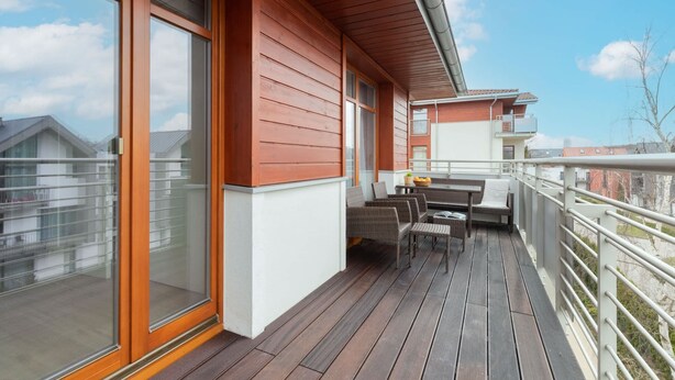 Una terraza de madera con una mesa, sillas, ventanas amplias y una barandilla.
