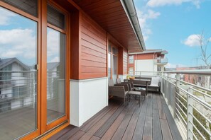 Una terraza de madera con una mesa, sillas, ventanas amplias y una barandilla.