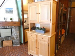 A wooden cabinet with drawers, a stone fireplace, and a tiled floor. - Charming Studio for 4 in Saint-Lary-Soulan - Near Slopes, Parking, South-West Exposure (Saint-Lary-Soulan)