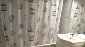 Kylpyhuone, jossa on meriteemaisilla kuvioilla koristellut suihkuverhot, pesuallas ja laatoitetut seinät.