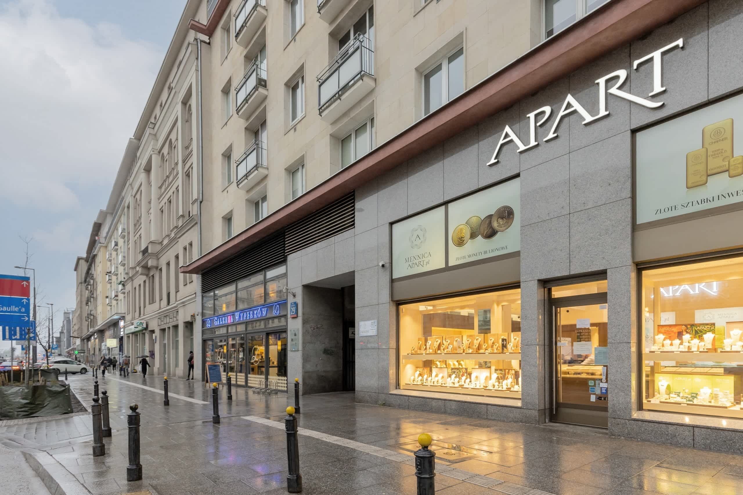 A building with a storefront labeled "APART" featuring a display of jewelry and a sign for "MENNICA APART".