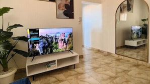 Un salon avec un téléviseur à écran plat posé sur un meuble, une grande plante en pot et deux tableaux abstraits accrochés au mur.