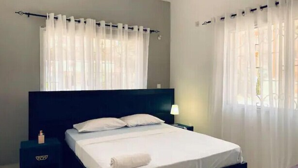 Une chambre à coucher avec un grand lit, une table de chevet, une lampe et des rideaux légers.