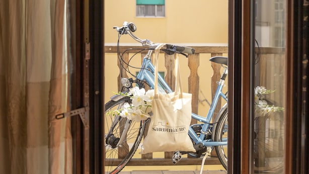 A bicycle with a white bag hanging from its rear rack, parked on a balcony with a wooden railing. - Foscolo 8 in Alghero (Alghero)