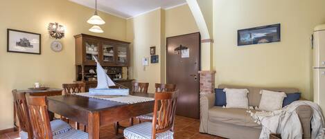 A dining area with a wooden table and chairs, a cabinet with glass doors, a sailboat model, and a sofa with pillows.