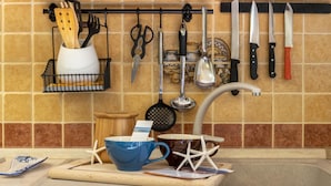 A kitchen with a tiled backsplash, a hanging utensil rack, and a wooden cutting board with a blue mug and starfish decoration. - Foscolo 8 in Alghero (Alghero)
