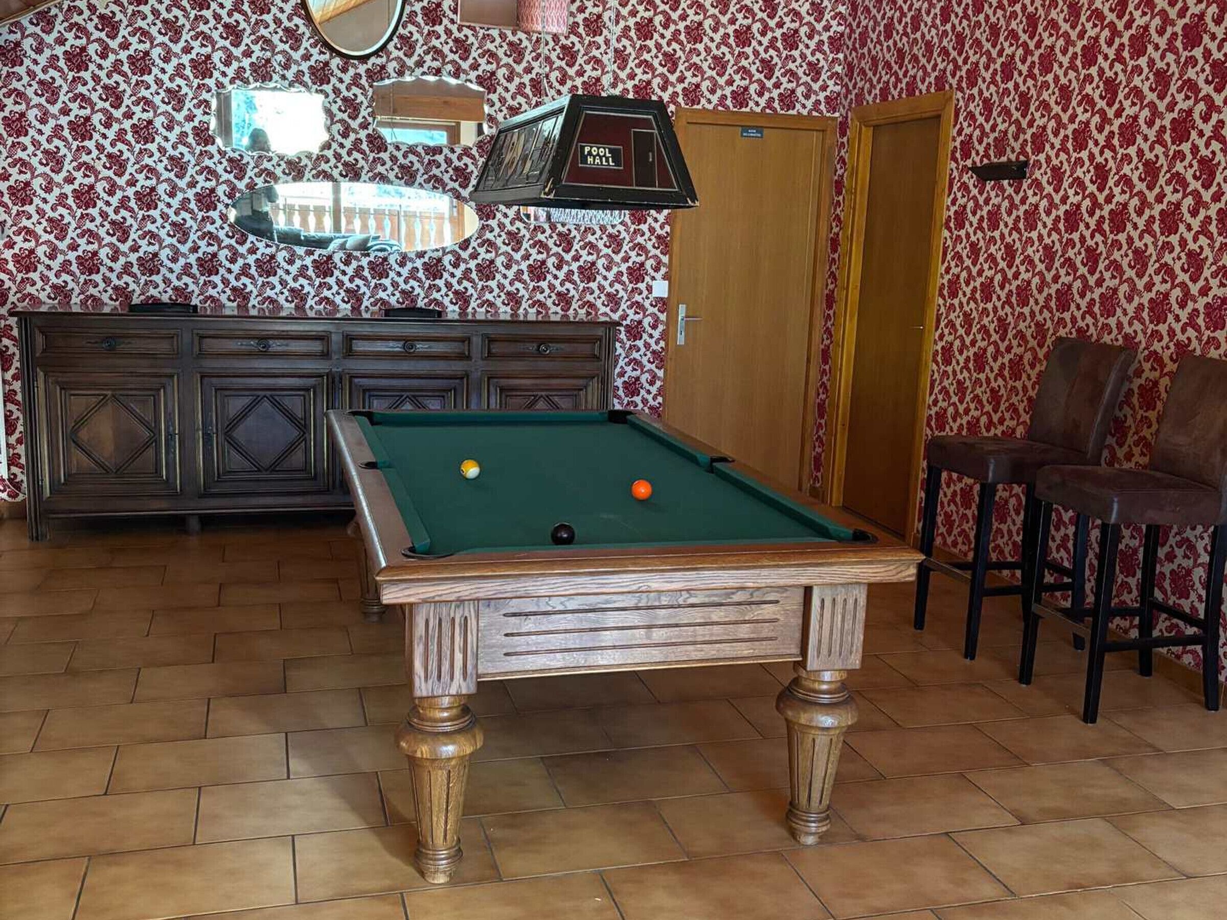 Una mesa de billar con bolas, un área de bar y una puerta que indica 'POOL HALL'.