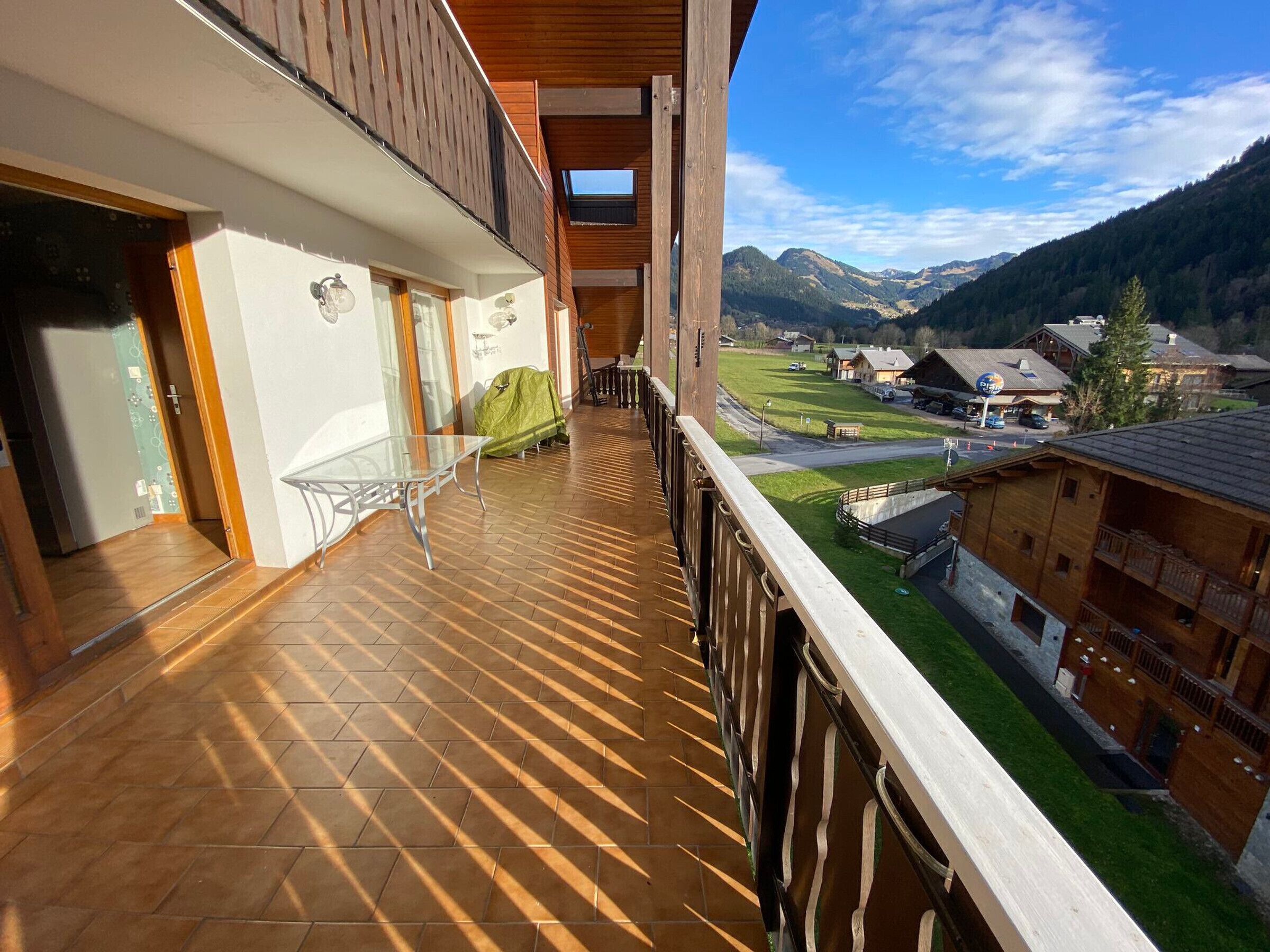 Varanda com vista para uma paisagem montanhosa, área de estar coberta ao ar livre e um edifício de madeira com um teleférico ao fundo.