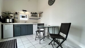 Cocina compacta con comedor, suelo de baldosas blancas y un reloj en la pared.