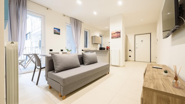 Een moderne woonkamer met een grijze bank, een houten bijzettafeltje en een aan de muur bevestigde televisie.