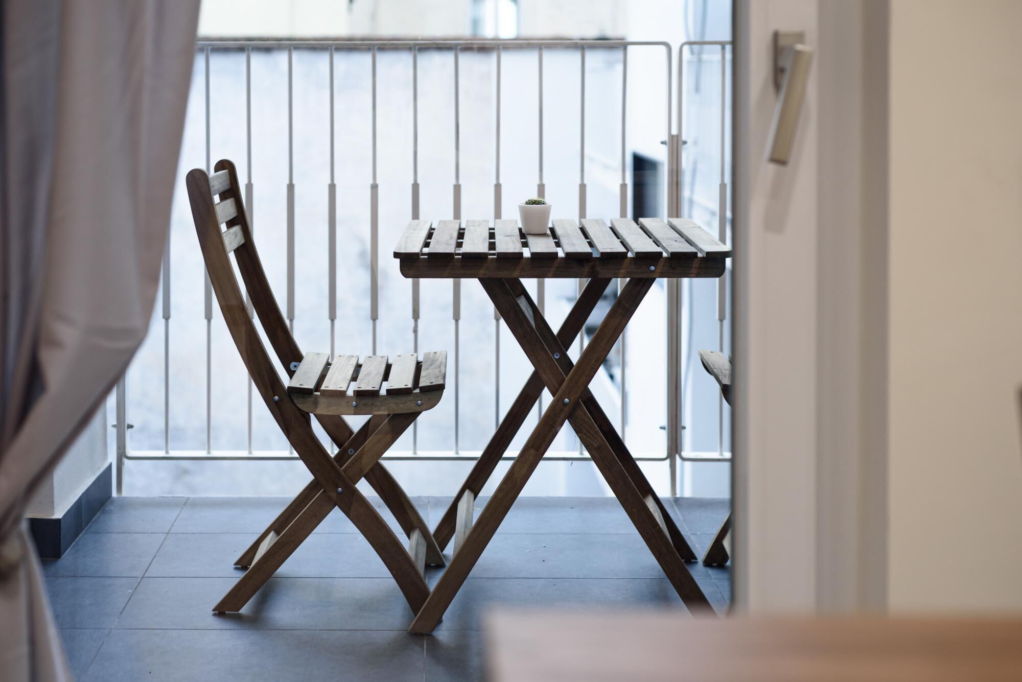 A wooden chair and table set on a balcony with a metal railing.