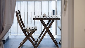Een houten stoel en tafel staan op een balkon met een metalen hekwerk.
