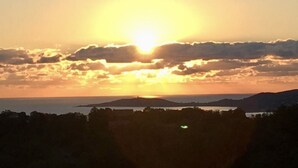 A sunset over a coastal landscape with a silhouette of trees and distant hills. - Atypical house with sea view (Porto-Vecchio)