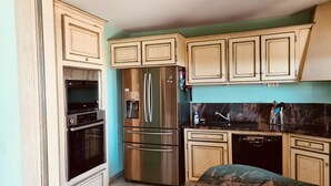 A kitchen with light wooden cabinets, stainless steel appliances, a marble countertop, and a sink. - Atypical house with sea view (Porto-Vecchio)