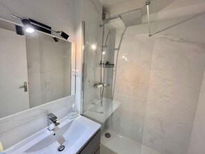 Ein modernes Badezimmer mit einer gläsernen Duschkabine, einem weißen Waschbecken und einem großen Spiegel.