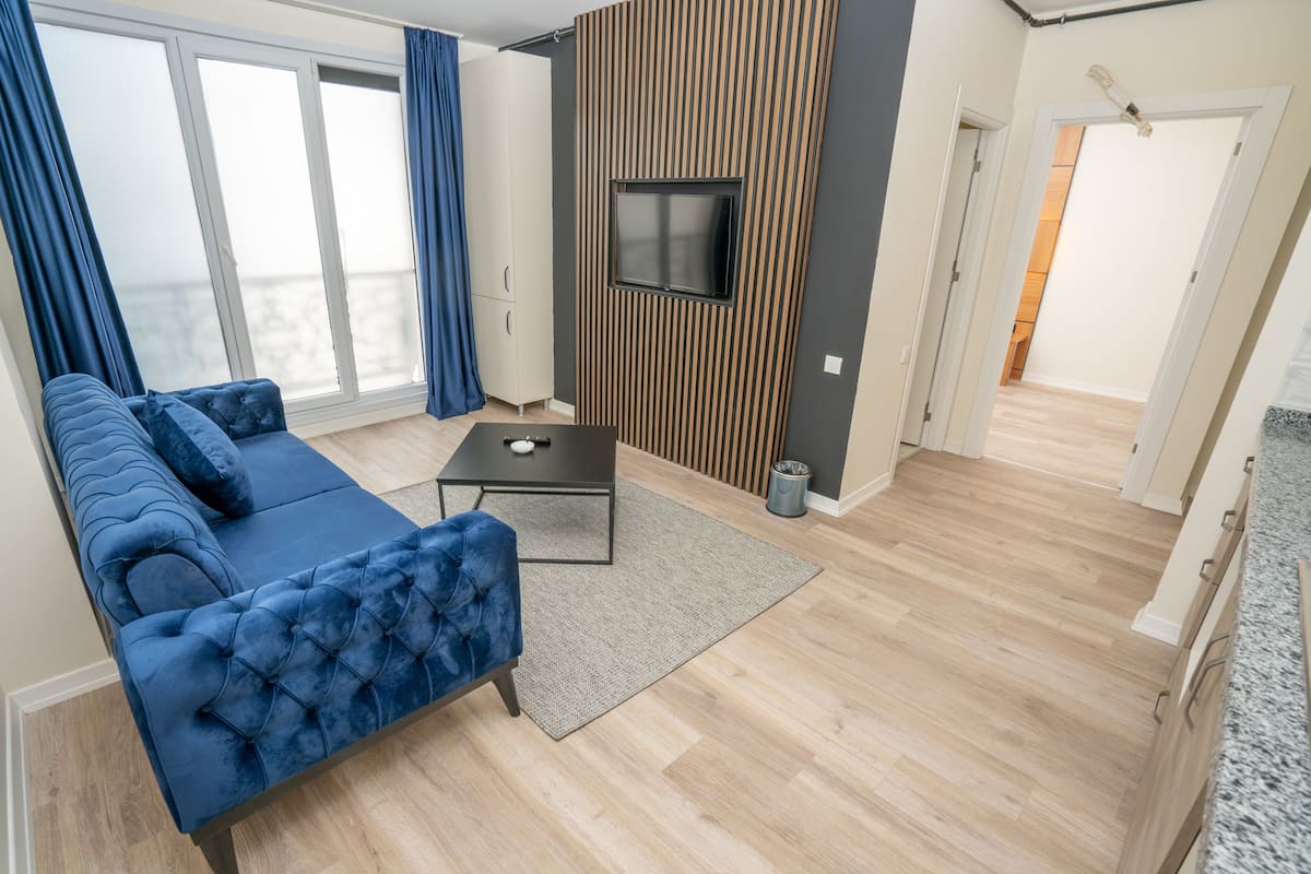 Una sala de estar moderna con un sofá azul, una mesa de centro y un televisor montado en una pared de madera.
