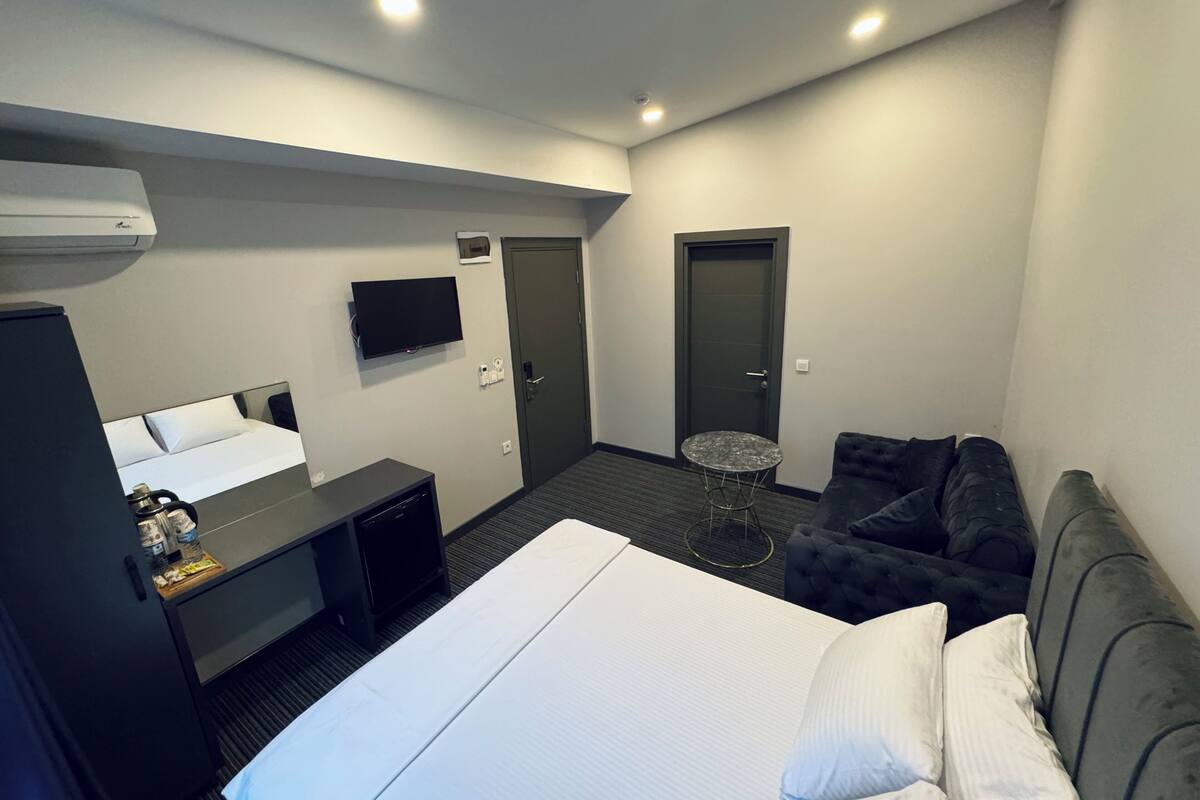 Una habitación de hotel con cama, escritorio, televisor, puerta y una pequeña mesa redonda.