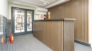 Aula, jossa on puupanelointi seinässä, vastaanottotiski ja lattialla palosammutin.
