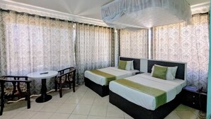 A hotel room with two beds, a round table, and curtains. - Alexander Hotel & Tours (Iringa)