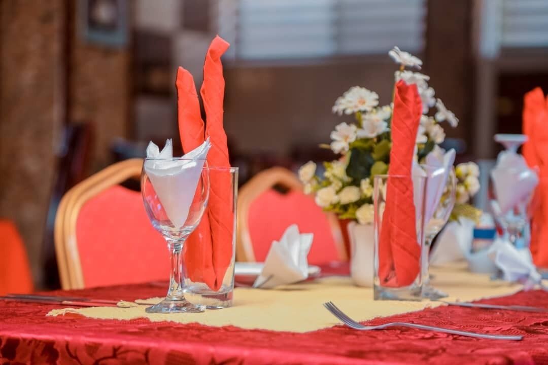 A dining table with red napkins, clear glassware, and a vase with flowers.