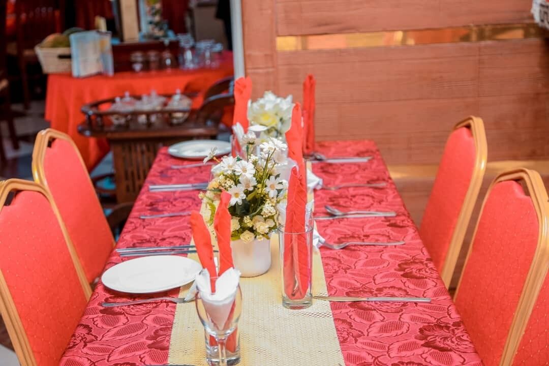Une table à manger dressée avec une nappe rouge, des assiettes blanches et des chaises orange.