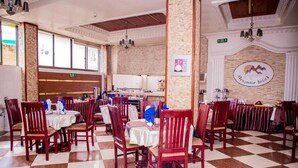 A restaurant with checkered flooring, wooden chairs, and tables set with white tablecloths. - Alexander Hotel & Tours (Iringa)