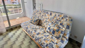 Une pièce avec un canapé, une fenêtre donnant sur des immeubles, un radiateur et un tableau accroché au mur.