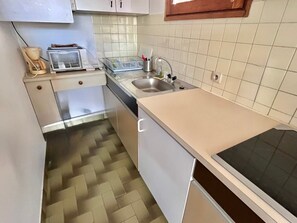 A compact kitchen with a microwave, toaster, sink, and a herringbone-patterned floor.