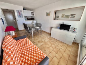 A compact living space with a sofa, a dining table, a kitchenette, and a TV on a cabinet.