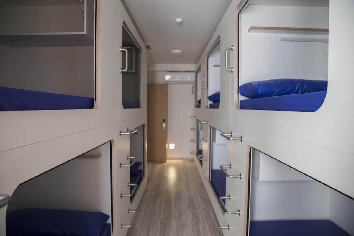 Un couloir étroit, avec des lits superposés de chaque côté, un plancher en bois et une porte au fond.