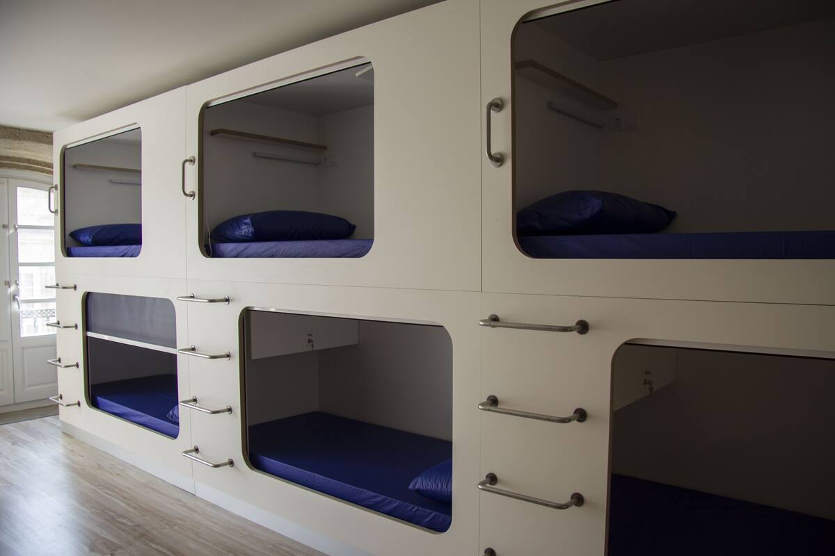 Une chambre avec des lits superposés, comprenant plusieurs lits, chacun étant équipé d’une fenêtre et de tiroirs.