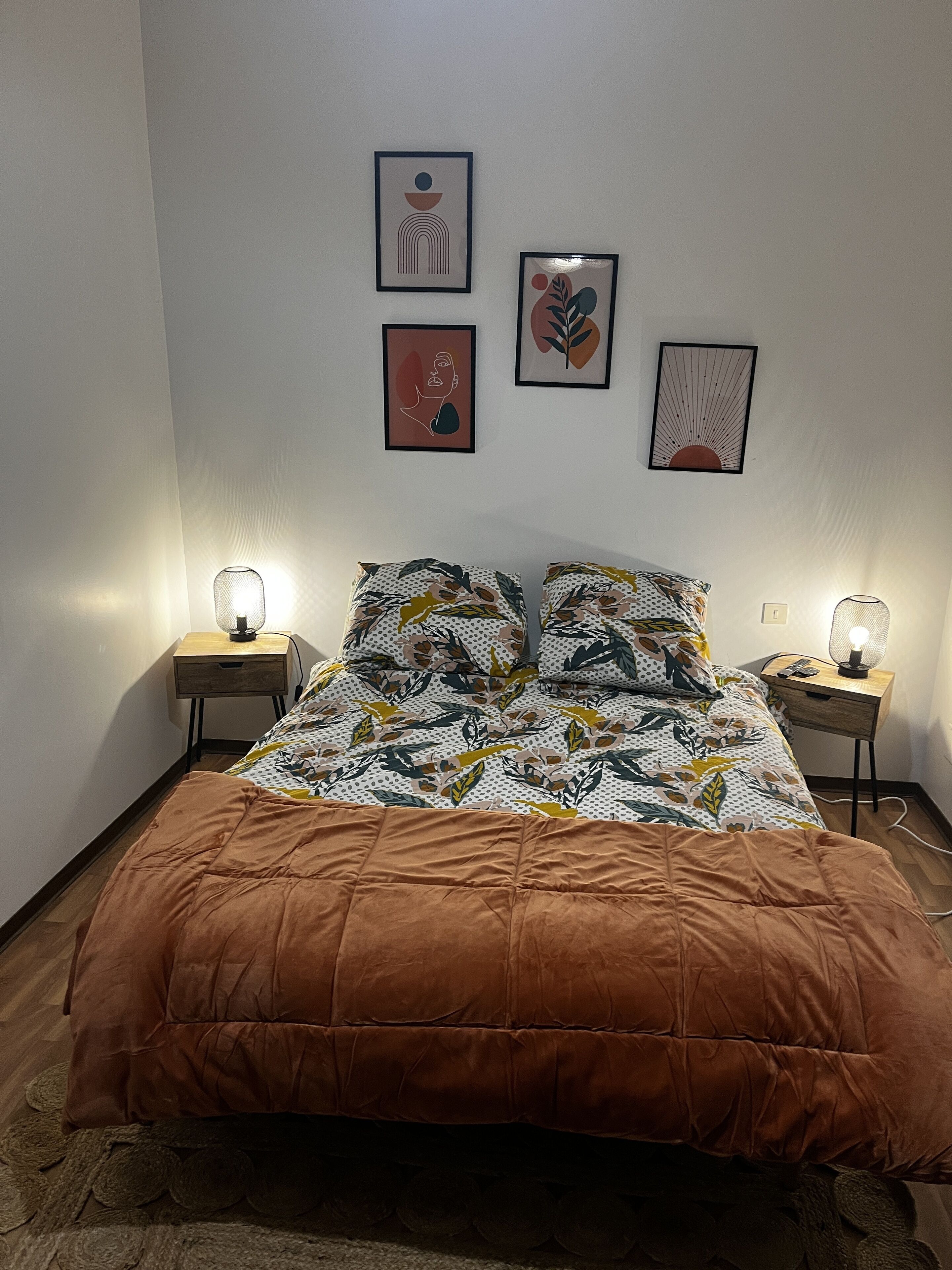 Ein Schlafzimmer mit einem Bett, zwei Nachttischen und drei an der Wand befestigten Kunstwerken.
