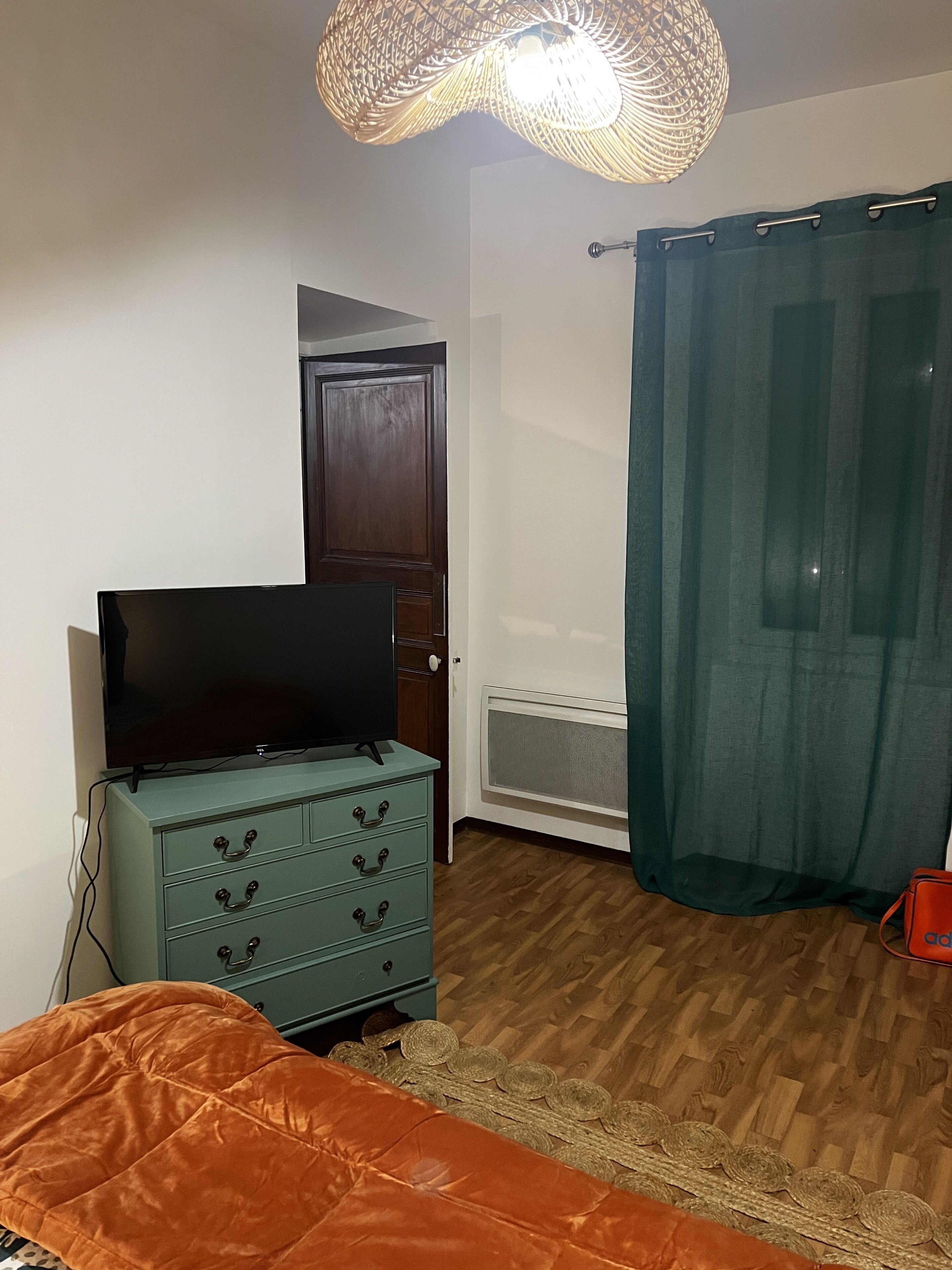 A room with a wooden floor, a television on a dresser, a door, and a curtain.